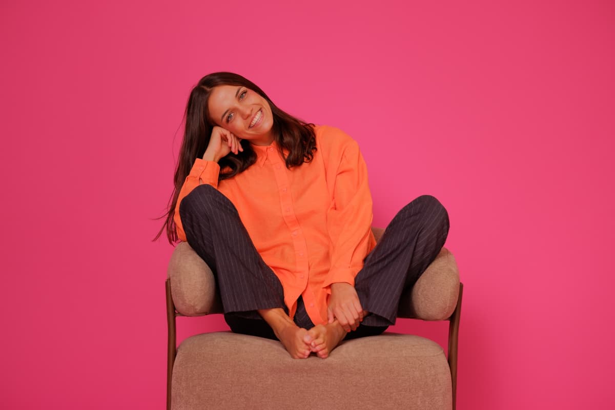 Pippi sonriendo, sentada en un sillón con camisa naranja sobre un fondo rosa