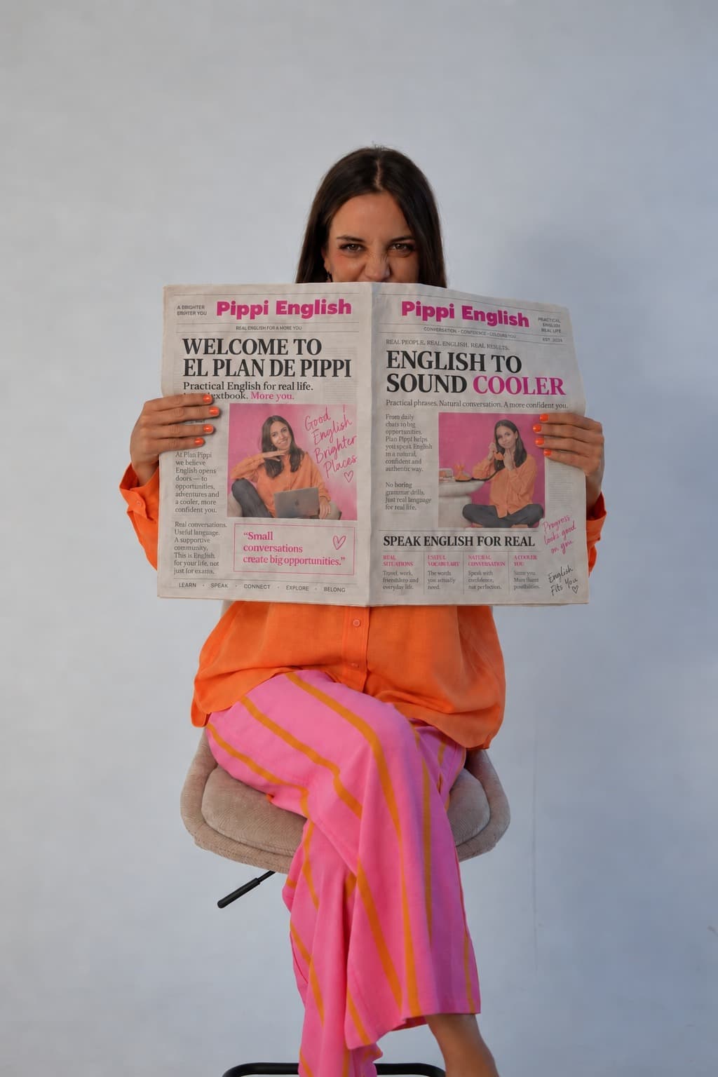 Pippi sentada con camisa naranja y pantalón rosa, sosteniendo el periódico de El Plan de Pippi